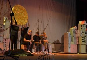 artyści na scenie, drzewo, słońce imitacje budynków z kartonu od lewej aktorzy niepełnosprawni na scenie